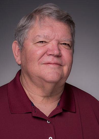 A Caucasian male with grey and black hair, Jim Poarch smiles at the camera and is wearing a maroon collared, button down dress shirt.